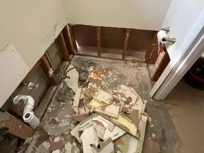 Bathroom stripped to the studs with the floor debris still in place after a sewage backup cleanup