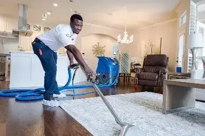 Restoration technician running an extraction wand across a soaked area rug in a living room during water removal