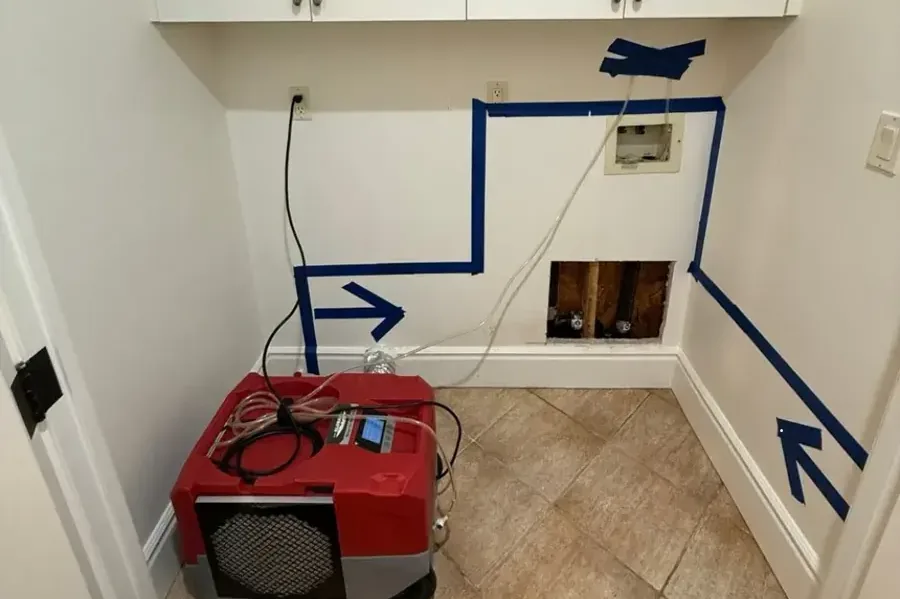Blue tape outlining the mapped wet zone on a laundry room wall while a dehumidifier runs
