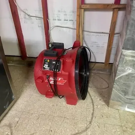 Red air mover drying a room where the lower wall was cut open and plastic sheeting hangs after a floor leak
