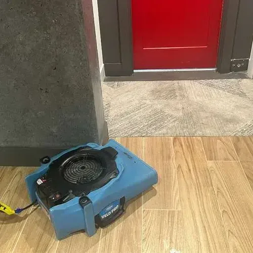 An air mover blowing across a wood look tile floor beside an open doorway