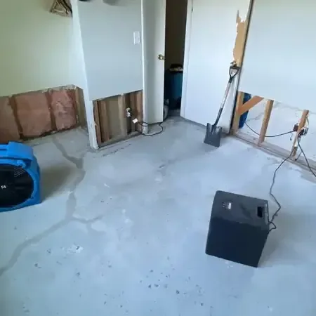Air movers and a dehumidifier running in a room with the lower drywall removed and the floor bare